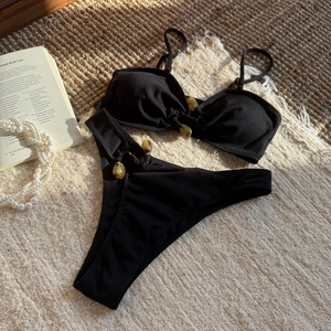 Flat lay of black ribbed bikini set with tortoiseshell rings on a woven texture mat
