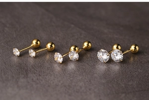 Detailed macro view of three pairs of gold screw-back stud earrings with round zircons