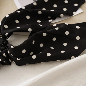Close-up of black and white polka dot fabric scrunchie with soft ribbon bow details