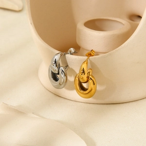 Detail of gold and silver chain link earrings hanging on a beige ceramic vessel