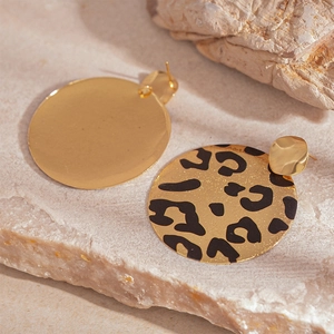 Détail de boucles d'oreilles rondes à motif léopard et finition dorée polie sur pierre