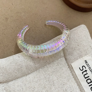 Macro shot of iridescent C-shaped bangle with ribbed texture on studio background