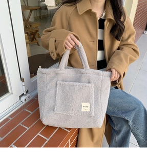 Close-up of a large grey plush lamb wool tote bag with a front pocket in an outdoor setting