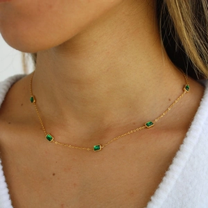 Detail of gold necklace featuring five rectangular emerald green zircon stones on model