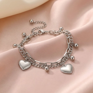 Detailed close-up of double-layer stainless steel heart charm bracelet on pink silk fabric