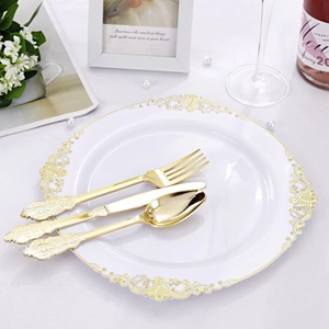 Elegant white disposable plate with gold pattern rim and gold cutlery set on tablecloth