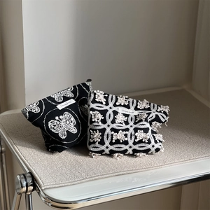 Detail of black canvas pouch with butterfly embroidery and white textured pom-poms