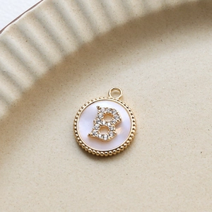 Close-up of gold plated round letter B pendant with zircon and white shell inlay