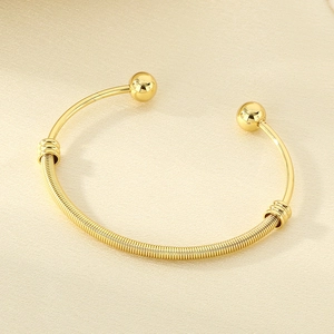 Close-up of 18K gold plated mesh bangle with spherical ends on champagne silk fabric