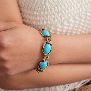 Detail of vintage gold bracelet with oval turquoise resin stones and twisted metal edges