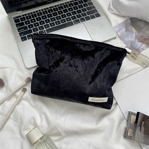 Detail of black velvet makeup bag with logo patch in a stylish flat lay aesthetic