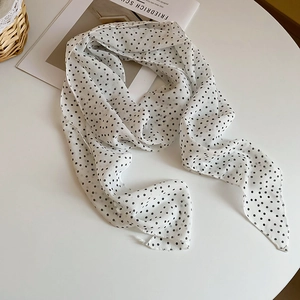 Flat lay of a white silk scarf with black polka dots on a minimalist white table