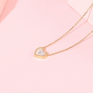 Détail d'un pendentif cœur doré avec incrustation blanche et petit zircon brillant au centre