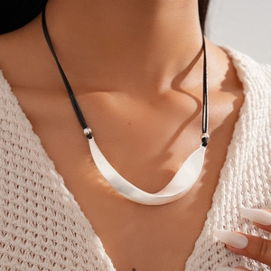 Detail of silver brushed geometric curved pendant on black cord over a beige knit sweater