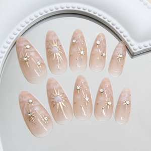 Nude pink marble almond press-on nails with golden starbursts and crystals on a mirror