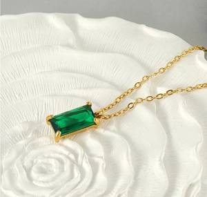 Detail of 18K gold-plated chain with square green zircon pendant on floral ceramic plate