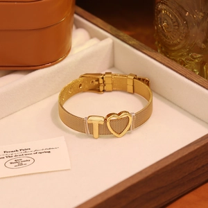 Gros plan du bracelet en maille dorée avec breloques cœur et lettre T sur velours