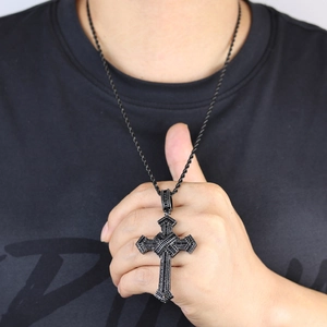 Detailed close-up of a black cross pendant with black stones on a black woven necklace cord