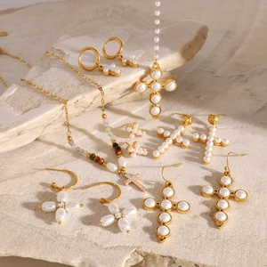 Close-up of golden cross earrings and pearl necklaces on a textured stone surface