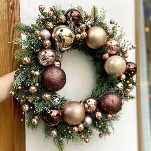 Christmas wreath with champagne gold ornaments and green pine needles on white wall