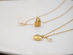 Gros plan de colliers en acier titane doré avec pendentifs cœur et cadenas ornés de perles