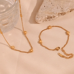 Detail of 18K gold-plated necklace and bracelet set with heart charms on fabric