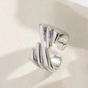 Detail of silver striped open ring with abstract lines on a textured beige surface