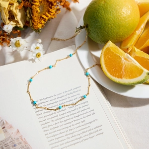 Détail d'un collier en acier titane doré avec des perles en pierre naturelle bleue sur un livre