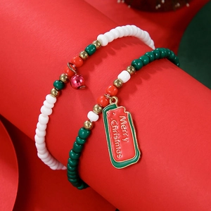 Detailed view of Christmas beaded bracelets with red enamel pendants and bells on red background