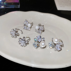 Detail of silver ear cuffs with pearls and zircon flower motifs on a white ceramic tray