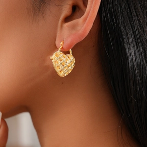 Close-up of a model wearing a gold hollow heart-shaped earring with textured pattern