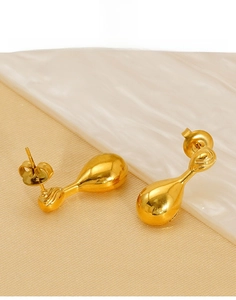 Close-up detail of golden water-drop titanium steel earring on marble background
