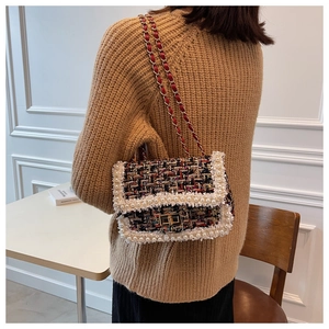 Close-up of elegant tweed crossbody bag with pearl trim and golden chain strap on a model