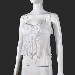 Detailed view of white pleated camisole with front tie and ruffle trim on mannequin