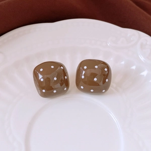 Detailed close-up of brown cube earrings with white polka dots on a ceramic plate