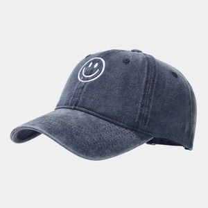 Close-up of embroidered white smiley icon on a grey washed denim baseball cap