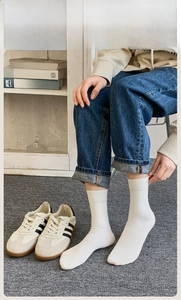 Detail shot of white ribbed mid-calf socks worn by a model in a cozy indoor setting