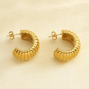Vue détaillée des boucles d'oreilles créoles dorées sur fond de soie beige texturé