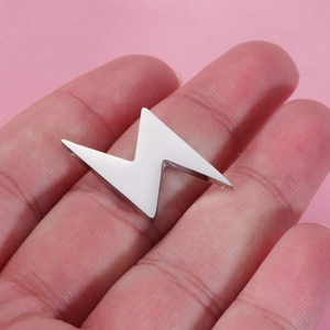 Detailed macro shot of a mini mirror-finish silver lightning bolt charm on a fingertip