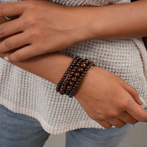 Detail of layered dark brown coconut wood beads bracelet on a knit sweater sleeve