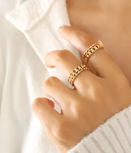 Detail eines goldenen Titanstahl-Kettenrings an der Hand mit weißem Strickhintergrund
