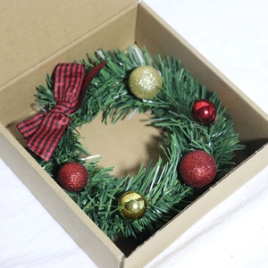Mini Christmas wreath with red black plaid bow and ornaments in a brown cardboard box
