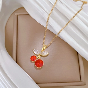 Detailed close-up of a sparkling red cherry pendant with crystal leaf on a gold chain
