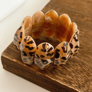 Close-up of leopard print resin bracelet on a dark wood base with polished oval links