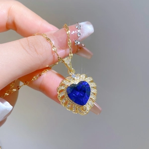 Close-up of a heart-shaped blue gemstone pendant with a gold chain held by fingers