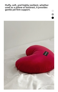 Detail of red heart-shaped plush pillow with branded tag on minimalist white bedding