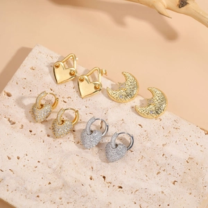 Detail view of heart and moon zircon earrings set on a travertine stone background