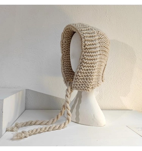 Détail d'un bonnet à oreilles en grosse maille beige avec de longs pompons décoratifs
