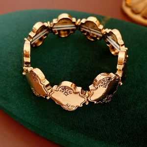 Gros plan d'un bracelet doré extensible avec motifs vintage sur support en velours