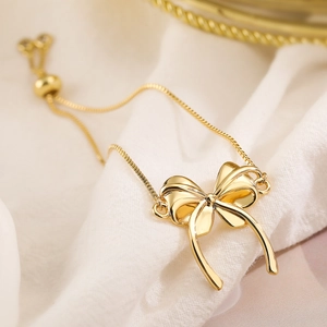 Detailed close-up of a gold bow pendant bracelet with adjustable pull-chain closure